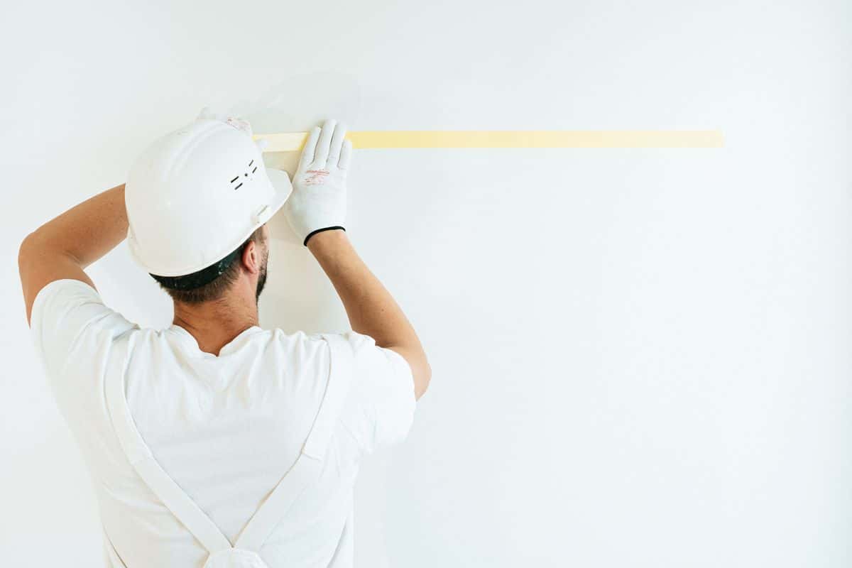 Maler klebt eine weiße Wand mit Kreppband ab — Beispielfoto